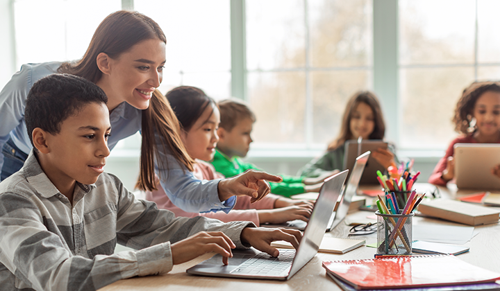 Eine Lehrerin zeigt Kindern eine Unterrichtsstunde auf einem Laptop.