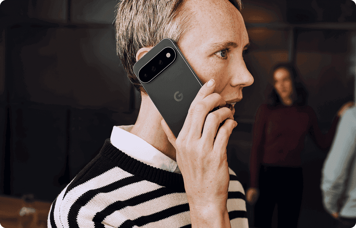 Person hält Smartphone mit Kameramodul am Ohr und führt ein Gespräch in moderner Umgebung