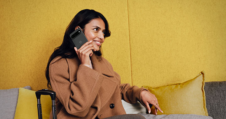 Woman in coat talking on smartphone relaxed on sofa with luggage in modern indoor setting