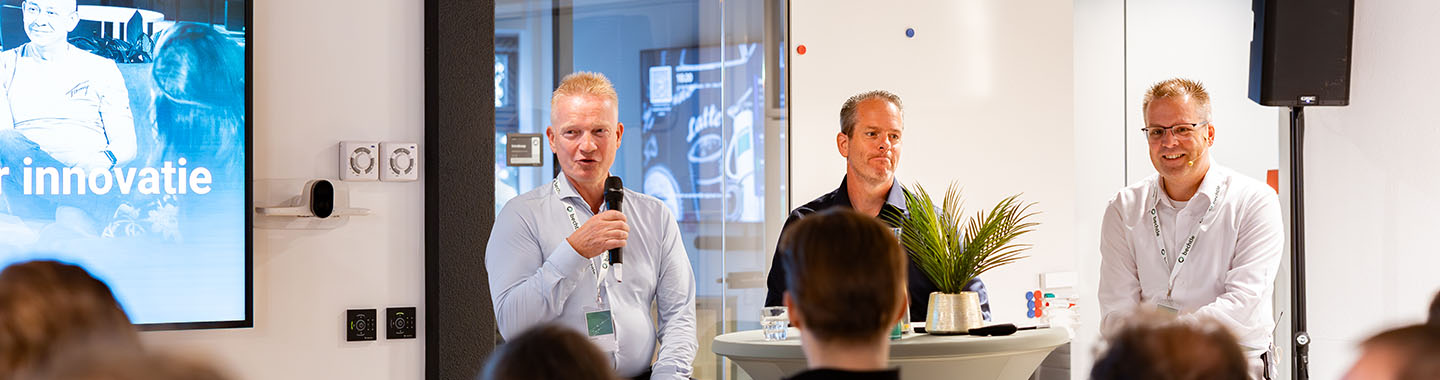 Three men conducting a panel discussion in a modern event space with an audience