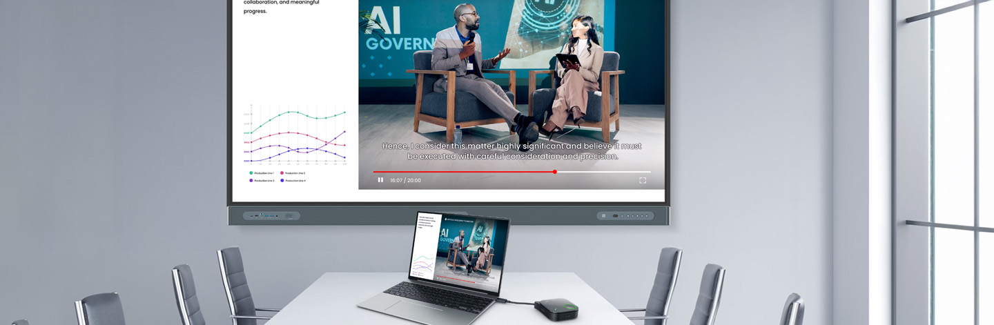 A meeting room with a large monitor showing two people and a graphic. In front of it is a table with a laptop and the BenQ InstaShow presentation system.