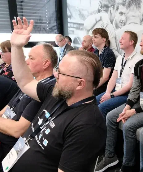 Ein Besucher sitzt im Publikum eines Vortrages und hebt die Hand um eine Frage zu stellen.
