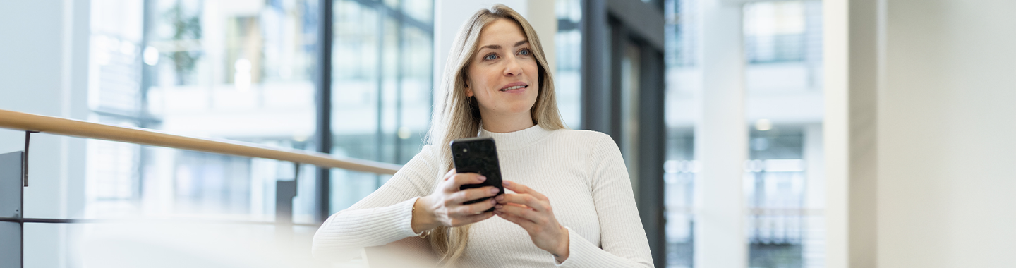 A woman sitting in an office and looking at the smartphone