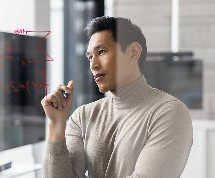 Mann in braunem Pullover schreibt mit Stift auf ein transparentes Board