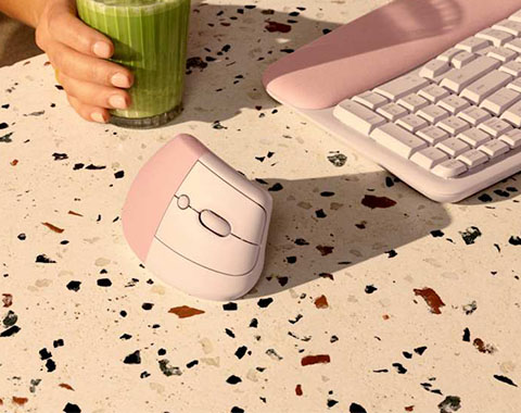 Ergonomic wireless mouse and keyboard in pastel colors on desk with hand holding green drink