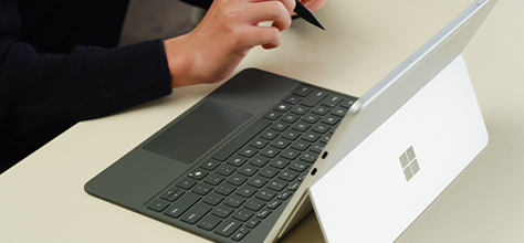 A close-up of a 12-inch Microsoft Surface Pro with a keyboard and Surface Pen, being used by a person at a desk.