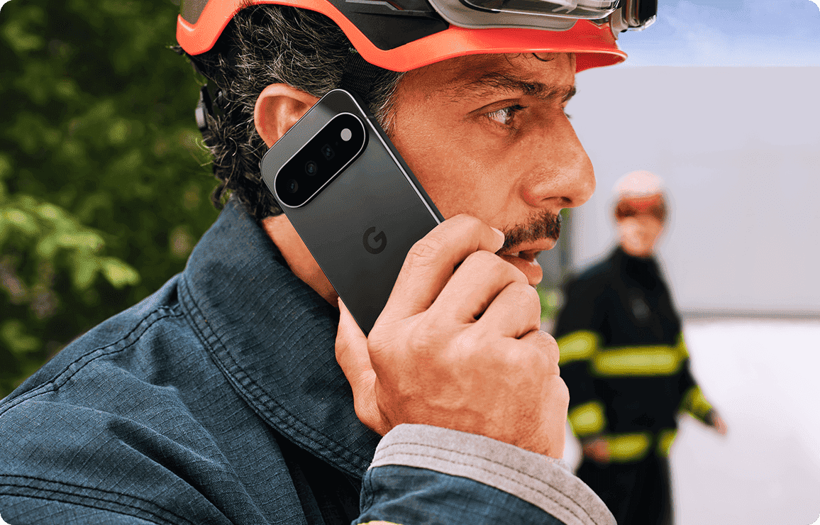 Feuerwehrmann mit Helm telefoniert konzentriert im Einsatz vor unscharfem Hintergrund mit zweiter Person