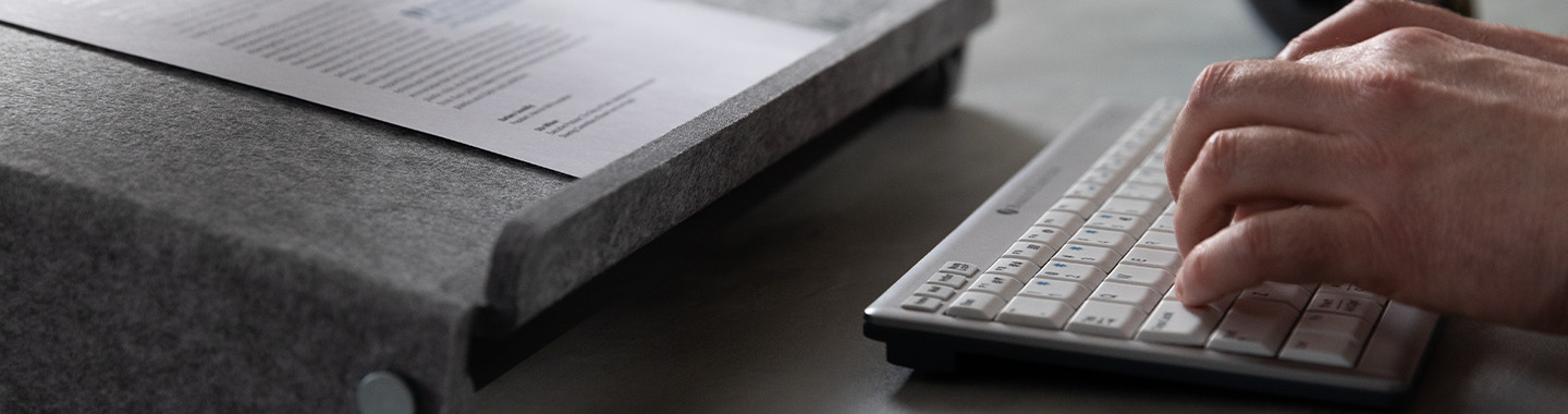 Hände tippen auf der Tastatur, davor eine Unterlage von dem Hersteller für Dokumente 