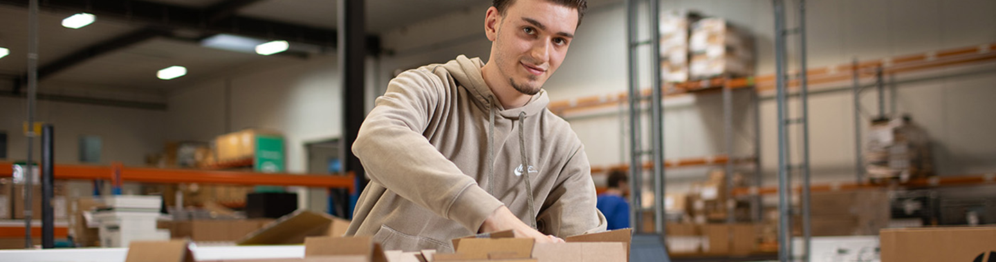 Mainbanner - Man packing goods into boxes in a warehouse with shelves in the background
