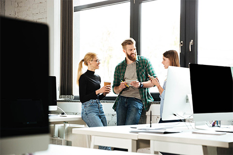 Three people in a modern office engaged in conversation and exchange during coffee break