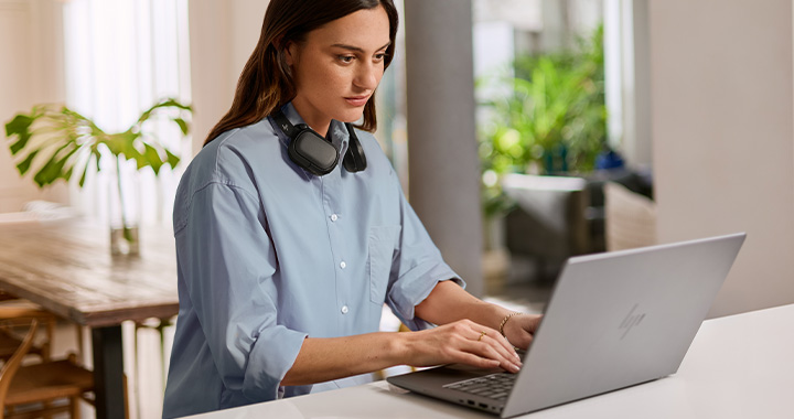 Woman working focused on laptop in bright, modern home office environment with headphones around her neck