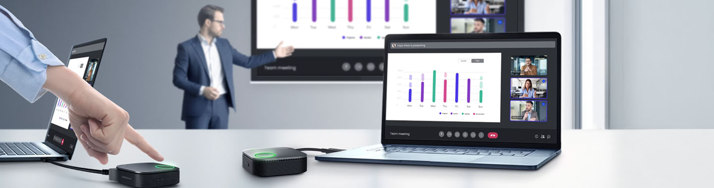 In the background, a man stands in front of a large screen giving a presentation. In the foreground, there is a table with two laptops and a hand pressing the BenQ InstaShow presentation button.