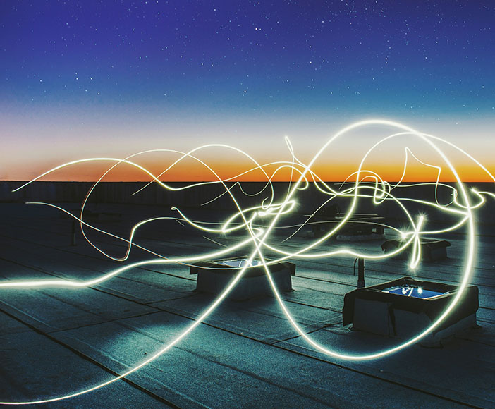 Light trails at dusk on a rooftop terrace with a clear horizon and urban background