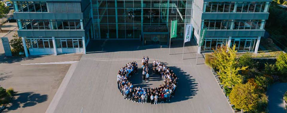 Große Gruppe von Mitarbeitenden vor modernem Bürogebäude