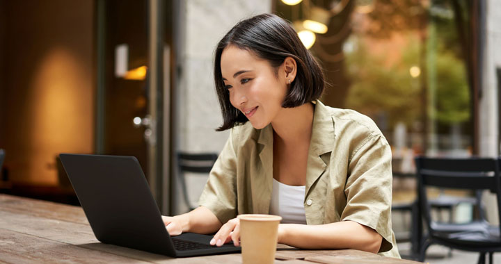A woman is sitting in a café, typing something on her laptop