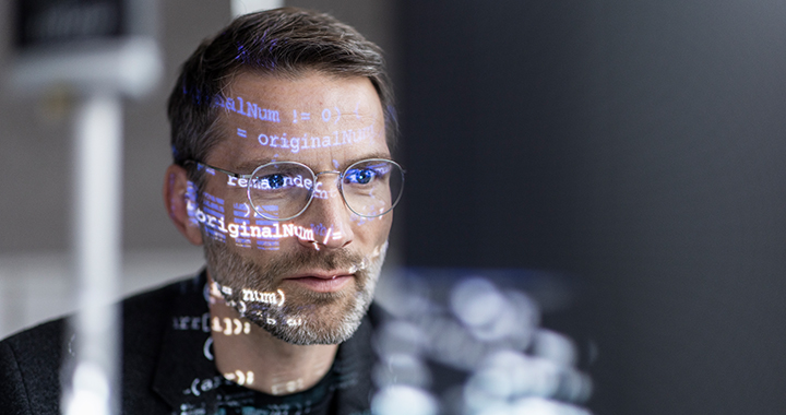 Nahaufnahme des Gesichts eines Mannes, in dem sich Code-Elemente von einem Bildschirm spiegeln.