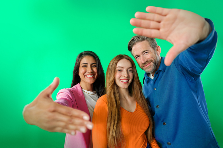 Drei Personen in freundlicher Pose vor grünem Hintergrund – einladende und positive Stimmung im Team