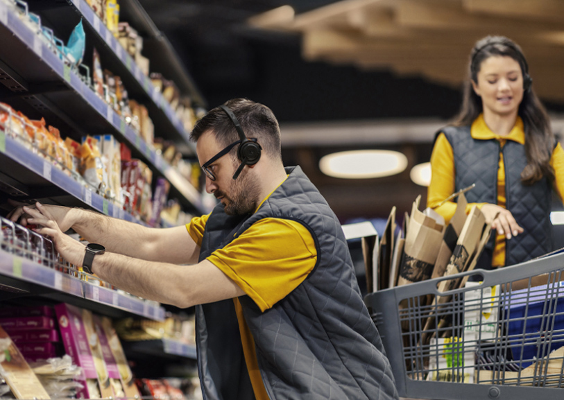 Jabra Perform 55 Headset neben einem Supermarktmitarbeiter, der mit Headset Warenregale auffüllt.