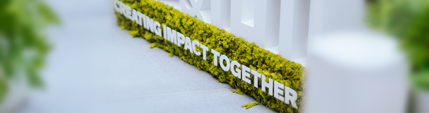Weiße Schrift mit dem Text ‚CREATING IMPACT TOGETHER‘ auf grünem Moos als nachhaltige Botschaft in moderner Umgebung