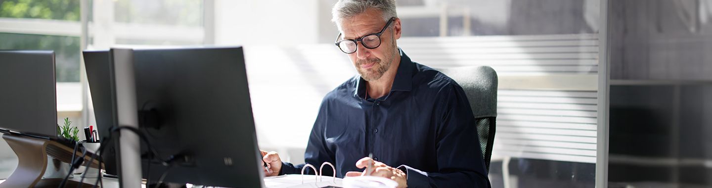 Mann arbeitet konzentriert an Dokumenten im modernen Büro mit Computer und natürlichem Licht