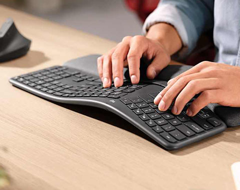 Person typing on ergonomic keyboard with integrated wrist rest at desk