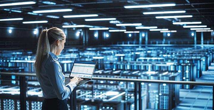 Eine Frau arbeitet an einem Laptop in einem Serverraum.