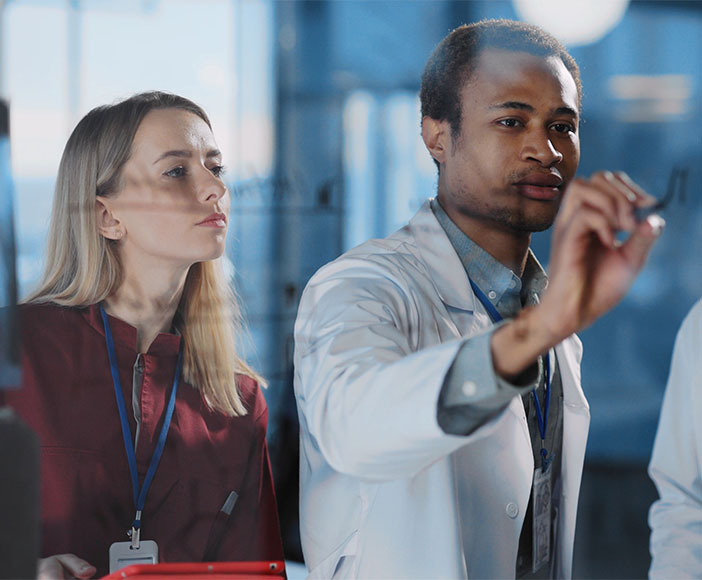 Frau schaut Arzt über die Schulter, während er etwas an eine Glastafel schreibt