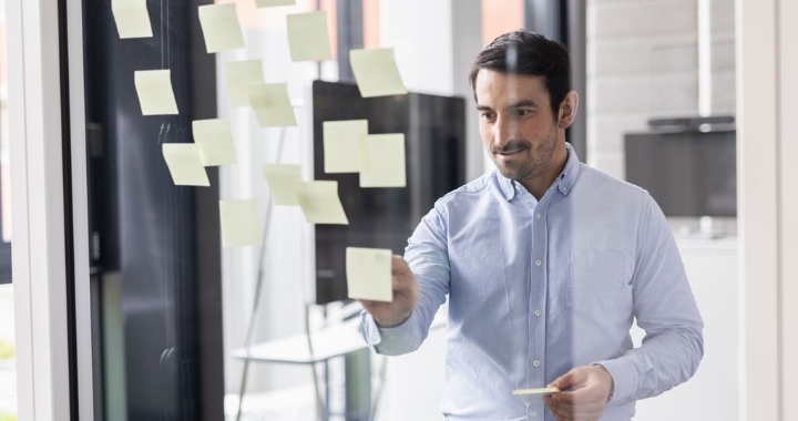 Mitarbeiter plant Projekt mit Post-it-Notizen an einer Glaswand im modernen Büro