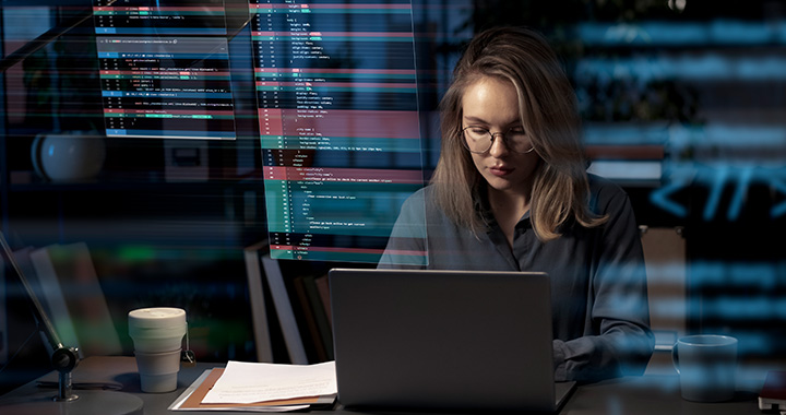 Woman working focused on laptop in dark environment with programming code on the screen
