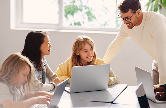 Der Lehrer hilft den Schülern, den Unterrichtsstoff auf dem Laptop zu verstehen.