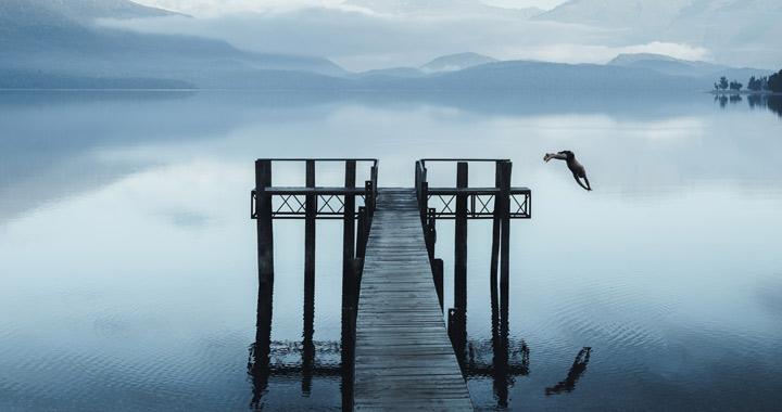 Person springt von einem Steg in einen Bergsee