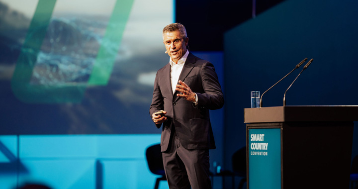Mann in Anzug hält Vortrag auf Konferenzbühne mit Fokus auf Smart Country Convention