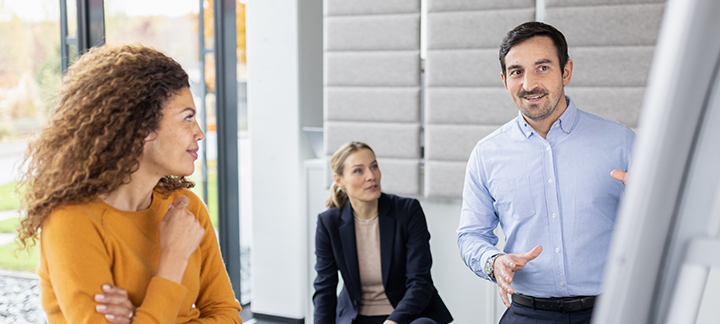 There are three people talking near a flipchart