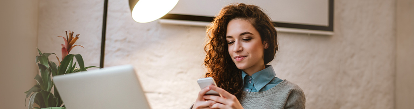 Frau vor einem Laptop mit Handy in der Hand