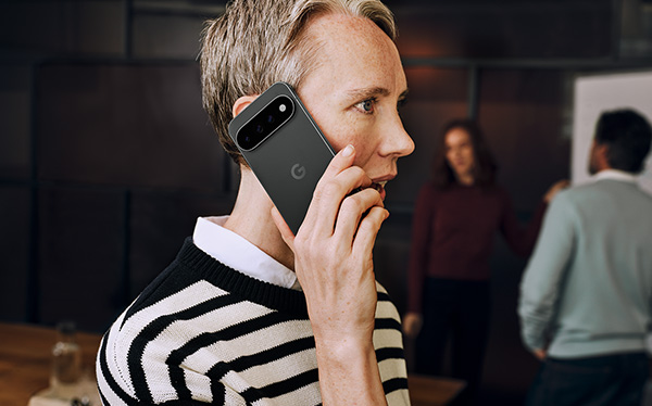 Person talking on smartphone in modern work environment with two other people in the background