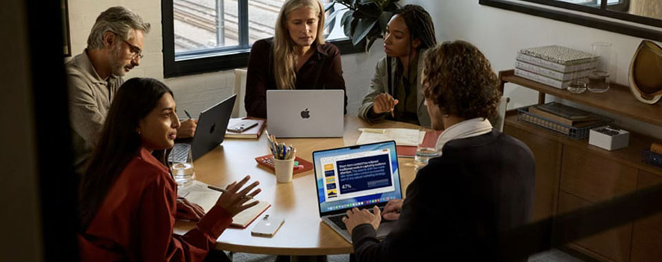 Four people in a meeting room collaborating on laptops and discussing presentation content