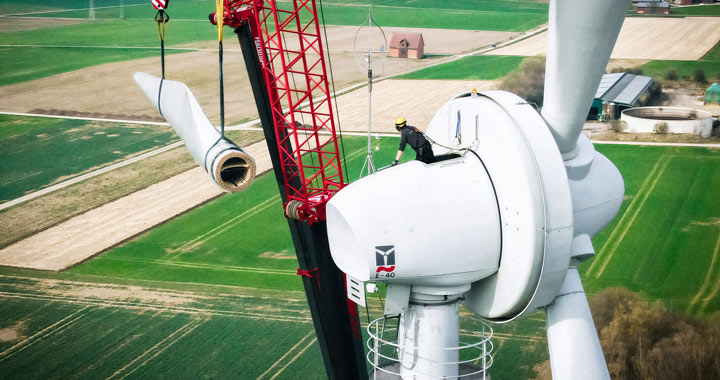 Techniker montiert Rotorblatt an Windkraftanlage mit Kran in ländlicher Umgebung
