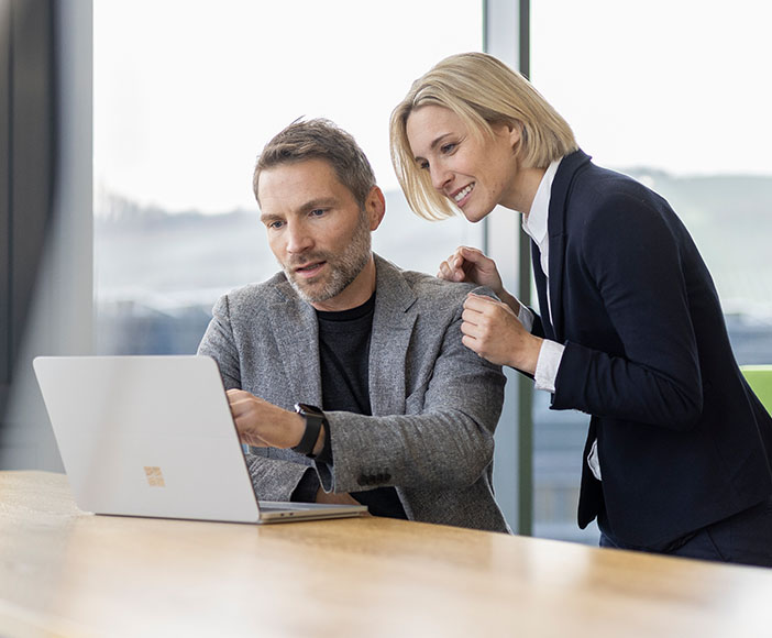 Mann und Frau sitzen im Büro und schauen in einen Laptop 