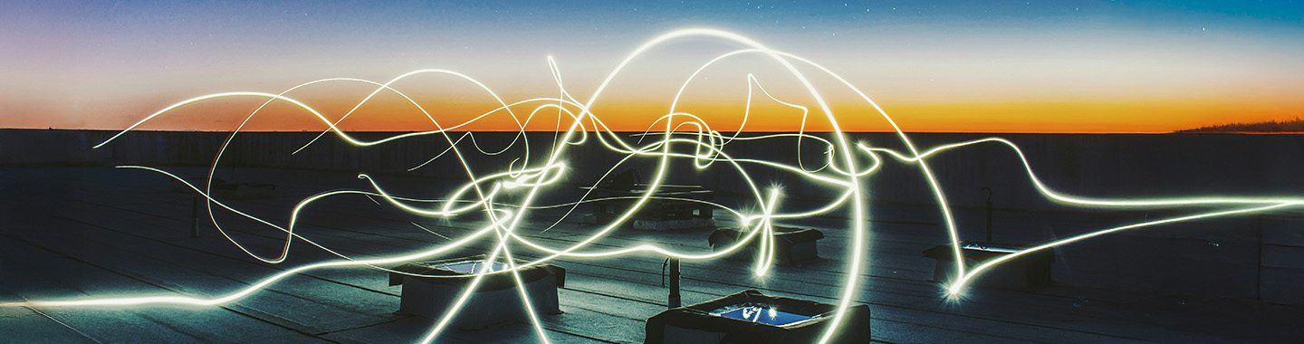 Lichtspuren in der Dämmerung auf einer Dachterrasse mit klar erkennbarem Horizont und urbanem Hintergrund