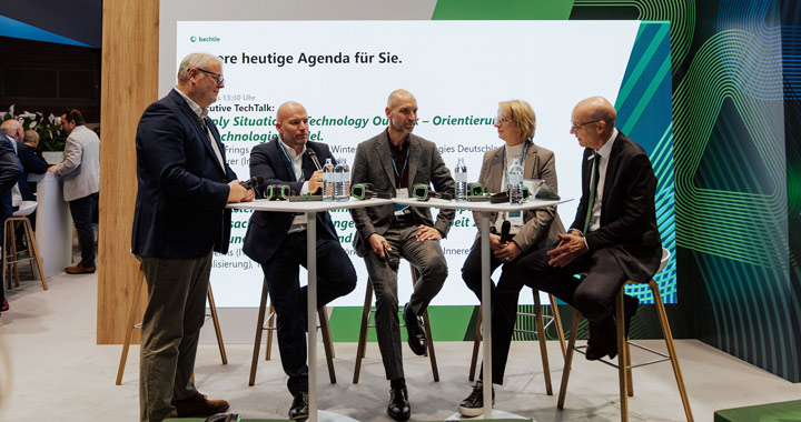 Fünf Personen im Gespräch an Stehtischen auf einer Fachmesse für Technologie und Digitalisierung