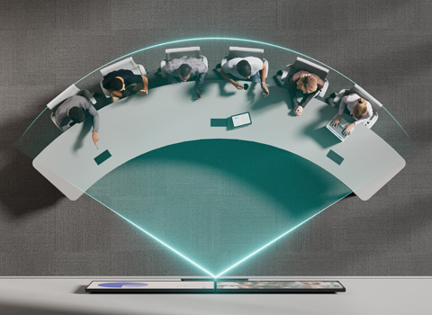 Personen sitzen an einem gebogenen Tisch und arbeiten gemeinsam an digitalen Geräten in moderner Arbeitsumgebung
