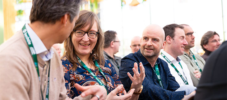 Several people engaged in conversation at an event wearing name badges and exchanging ideas