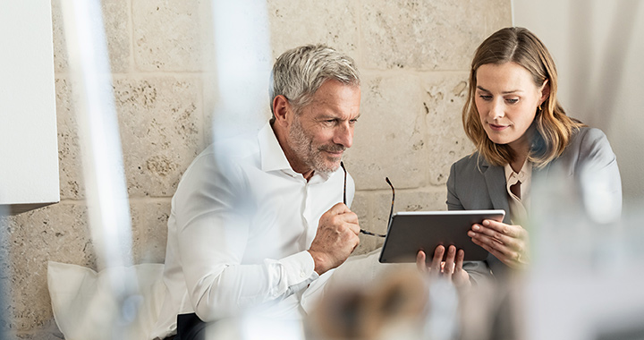 Zwei Personen im modernen Büro betrachten gemeinsam ein Tablet und besprechen digitale Inhalte
