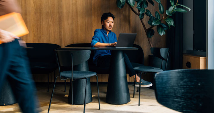 A man is sitting in a café, typing something on his laptop
