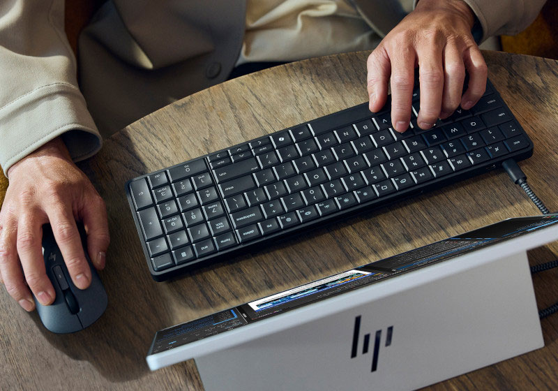 A young man is working on an HP EliteBook in front of a screen (view from above)