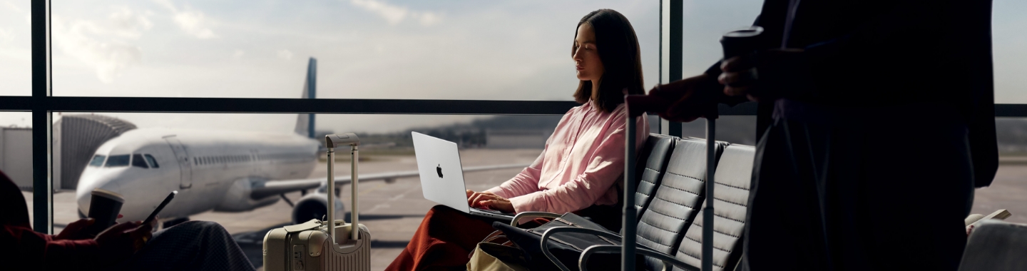 Eine Frau sitzt an einem Flughafen und arbeitet an einem MacBook.