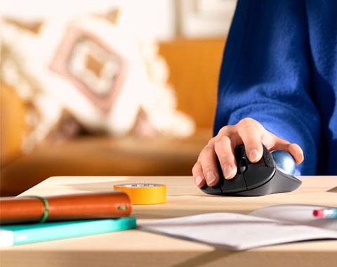 Person's hand operating a computer mouse at a desk with office supplies in the background