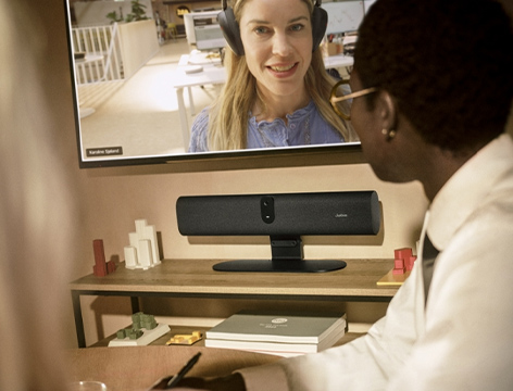 A person is participating in a video conference, while a Jabra Panacast U30 video bar mounted beneath the monitor facilitates communication.
