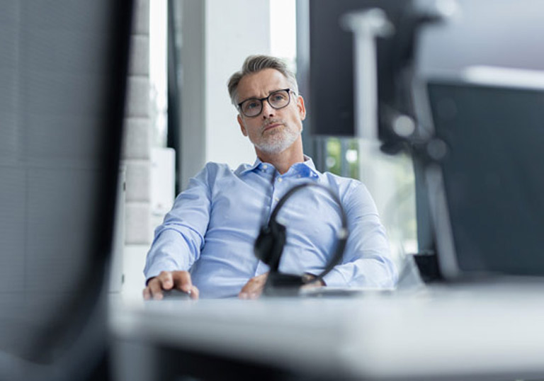 Mann im Büro sitzt am Schreibtisch und blickt konzentriert in die Kamera, moderne Arbeitsumgebung