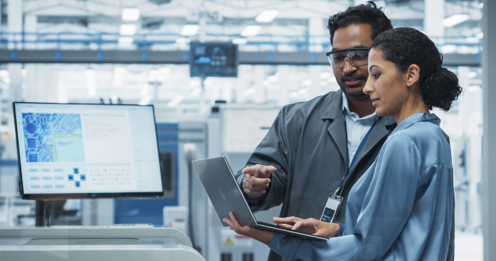 Ein Mann und eine Frau überprüfen in einer Industriehalle Daten auf einem Laptop.